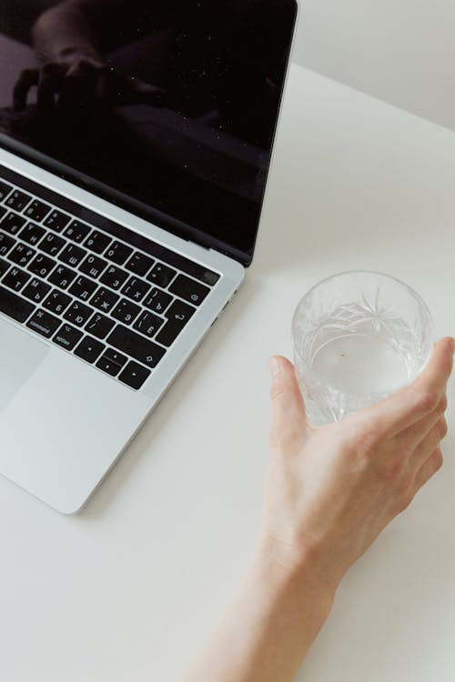 A person holding a glass of water near a laptop, showing the risk of accidental liquid spills on electronics